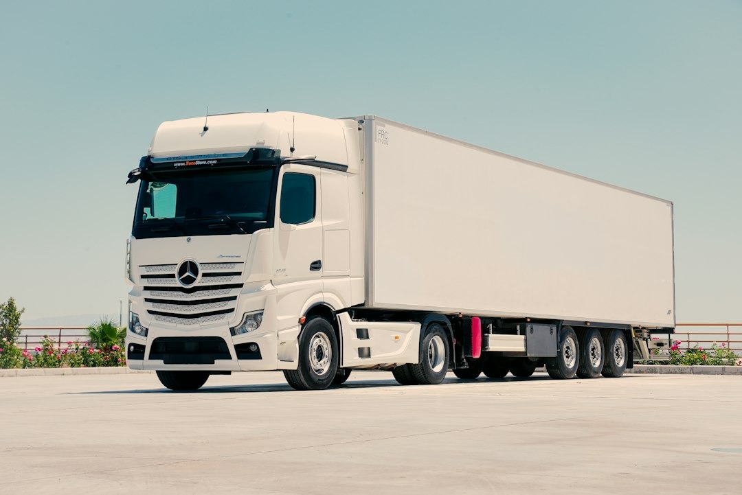 White semi-truck with refrigerated trailer parked on concrete lot.